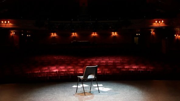 Ein Stuhl steht allein auf einer sonst leeren Bühne in einem leeren Theatersaal.