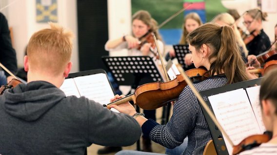 Schülerinnen und Schüler musizieren mit Geigen und anderen Instrumenten während des Unterrichts.