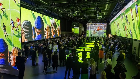 Besucherinnen und Besucher der Ausstellung „In Motion“ betrachten Kunstwerke fußballspielender Menschen auf LED-Tafeln.