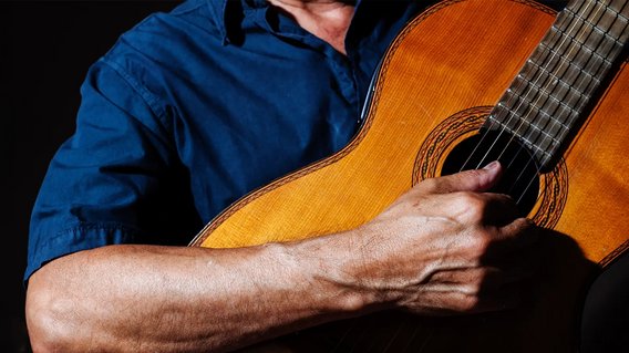 Eine menschliche Hand im Vordergrund spielt die klassische Gitarre.